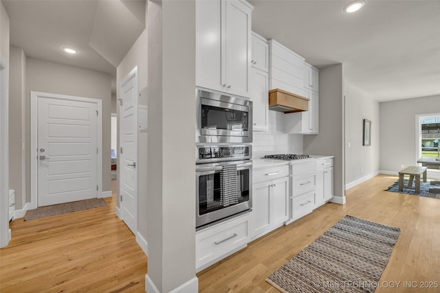 kitchen with light hardwood / wood-style flooring, appliances with stainless steel finishes, backsplash, and white cabinetry