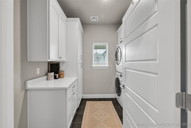 laundry room featuring cabinets, dark tile patterned flooring, and stacked washer / drying machine