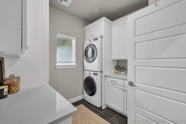 laundry room with cabinets, stacked washer / drying machine, and dark tile patterned flooring