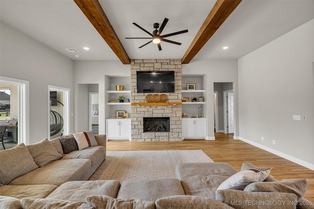 living room featuring ceiling fan, a fireplace, beam ceiling, light hardwood / wood-style flooring, and built in shelves