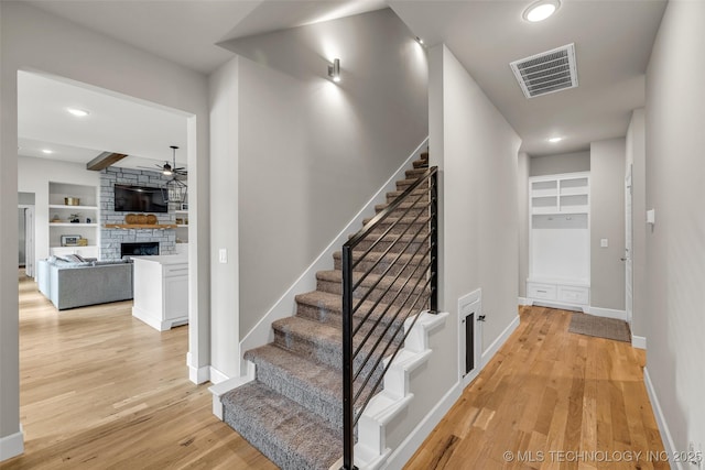 staircase featuring built in shelves, ceiling fan, a fireplace, and hardwood / wood-style floors