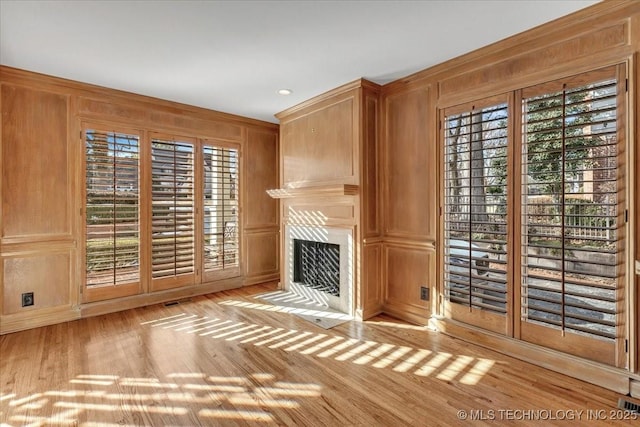 unfurnished living room featuring a fireplace with flush hearth, a healthy amount of sunlight, light wood-style floors, and wooden walls