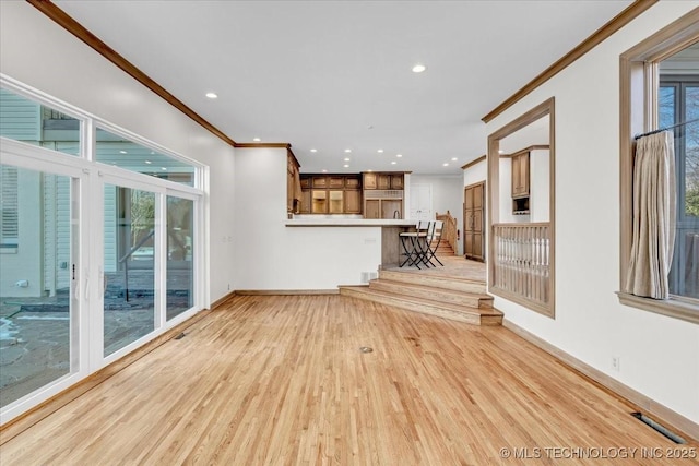 unfurnished living room with ornamental molding, baseboards, plenty of natural light, and light wood finished floors