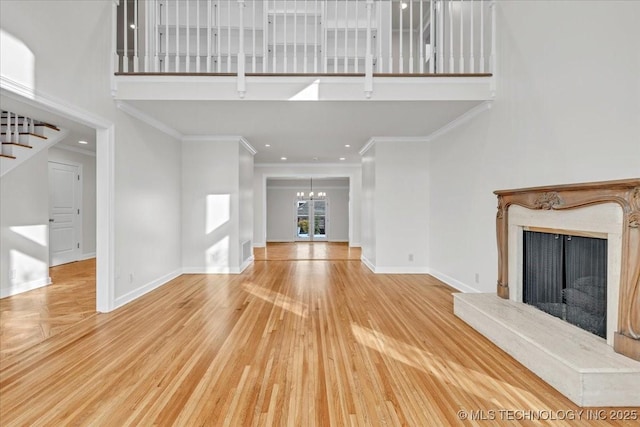 unfurnished living room featuring a high ceiling, wood finished floors, a high end fireplace, baseboards, and stairway