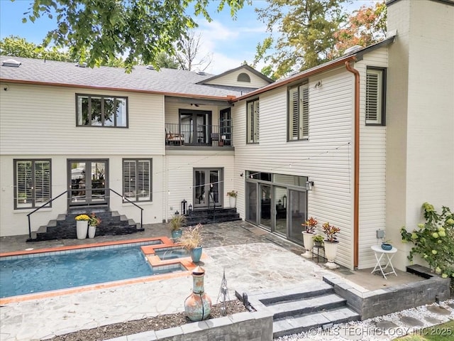 back of property featuring french doors, entry steps, a patio area, a balcony, and an outdoor pool