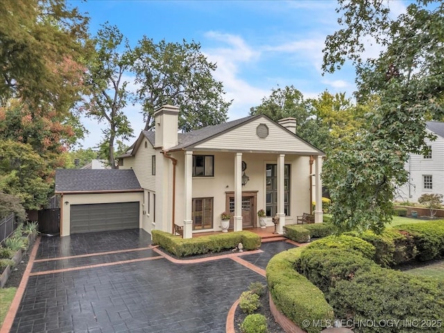 greek revival inspired property with decorative driveway, a chimney, a porch, fence, and a garage