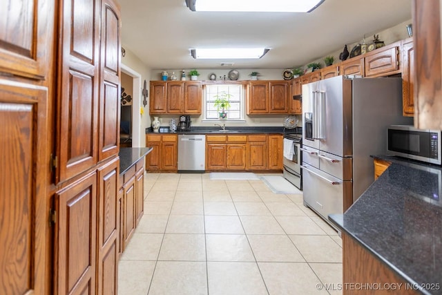 kitchen with sink, dark stone countertops, stainless steel appliances, and light tile patterned flooring