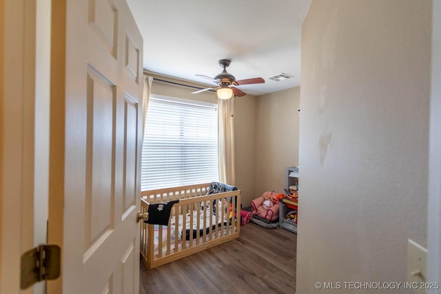 bedroom with ceiling fan, a crib, and hardwood / wood-style flooring