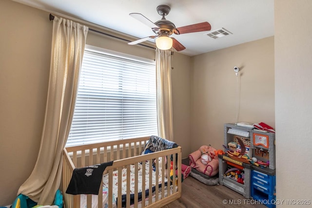 bedroom featuring ceiling fan, wood-type flooring, and a crib