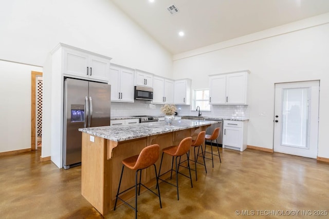 kitchen featuring high vaulted ceiling, white cabinets, stainless steel appliances, and a kitchen island