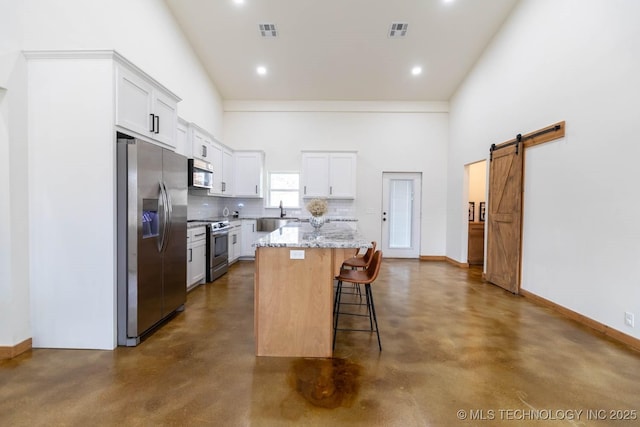 kitchen with a barn door, a kitchen island, appliances with stainless steel finishes, a breakfast bar area, and light stone counters