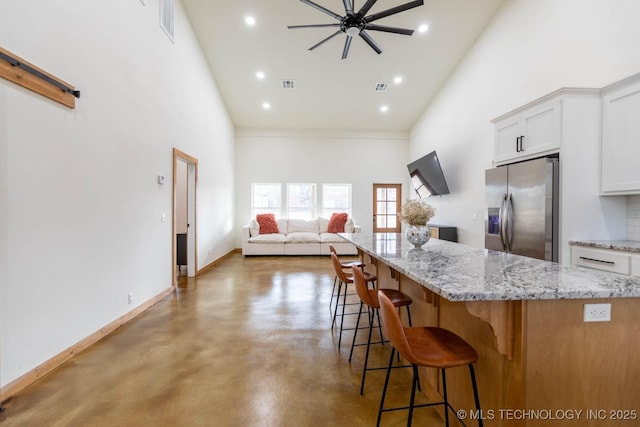 kitchen with white cabinetry, stainless steel fridge, a kitchen island, a towering ceiling, and concrete flooring