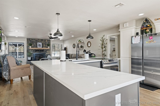 kitchen featuring appliances with stainless steel finishes, decorative light fixtures, a large island, ceiling fan, and light hardwood / wood-style flooring