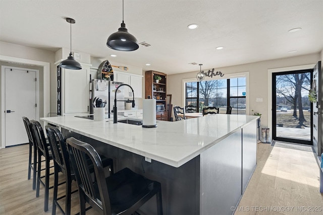 kitchen featuring white cabinetry, light hardwood / wood-style floors, a spacious island, decorative light fixtures, and light stone countertops