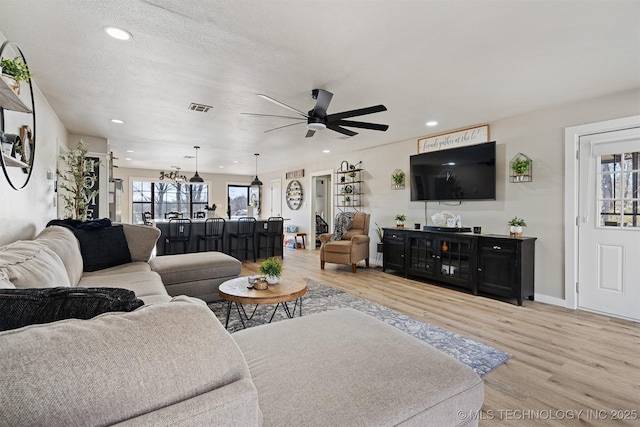 living room with light wood-type flooring, ceiling fan, and a textured ceiling