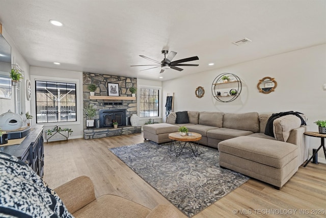 living room with ceiling fan, a stone fireplace, and light hardwood / wood-style flooring