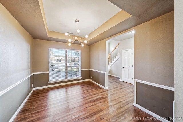 unfurnished room with wood-type flooring, a raised ceiling, and a notable chandelier