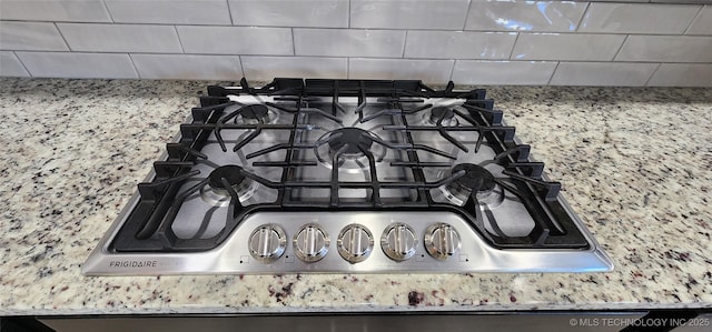 details featuring stainless steel gas cooktop, decorative backsplash, and light stone countertops