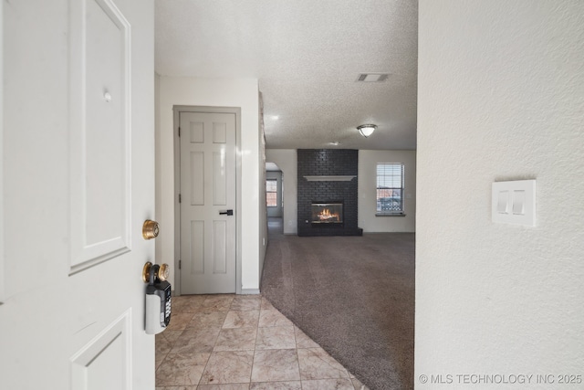 hallway with visible vents, light colored carpet, and a textured ceiling