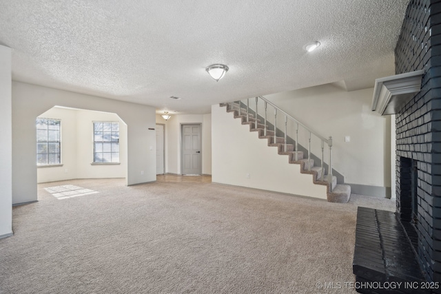 unfurnished living room with a brick fireplace, a textured ceiling, and carpet