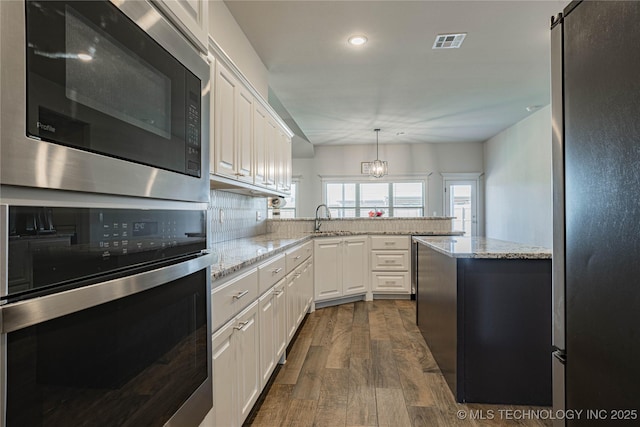 kitchen featuring appliances with stainless steel finishes, decorative light fixtures, white cabinetry, backsplash, and dark hardwood / wood-style floors