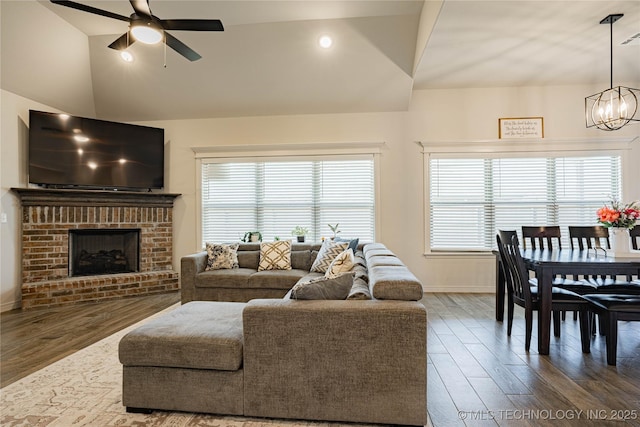 living room with wood-type flooring, plenty of natural light, ceiling fan with notable chandelier, and a brick fireplace