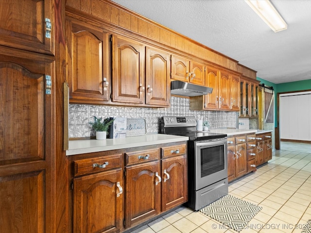 kitchen featuring a barn door, backsplash, light tile patterned flooring, stainless steel electric range oven, and a textured ceiling