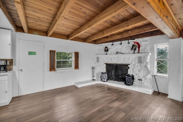 unfurnished living room with wood ceiling, beamed ceiling, a stone fireplace, and dark hardwood / wood-style floors