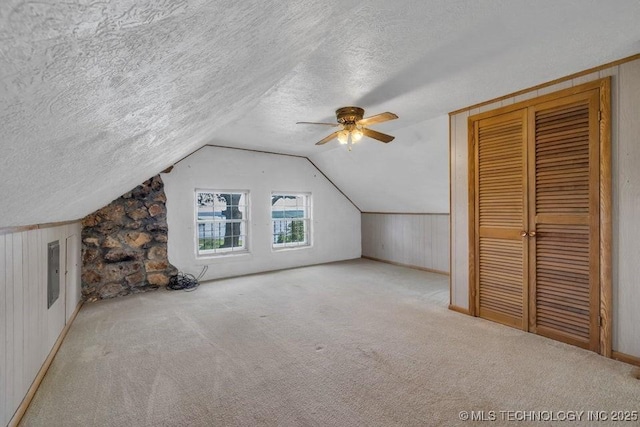 additional living space with light carpet, wood walls, ceiling fan, lofted ceiling, and a textured ceiling