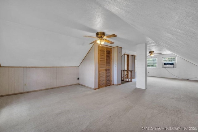 bonus room with ceiling fan, a textured ceiling, light carpet, and wood walls