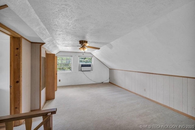 bonus room featuring light carpet, wood walls, ceiling fan, a textured ceiling, and vaulted ceiling