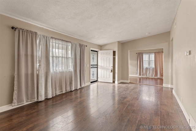 empty room with a textured ceiling, dark hardwood / wood-style flooring, and lofted ceiling