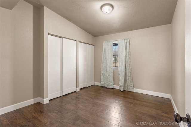 unfurnished bedroom featuring vaulted ceiling, dark hardwood / wood-style floors, a textured ceiling, and two closets