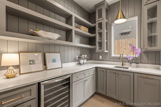 kitchen with beverage cooler, decorative light fixtures, sink, gray cabinets, and light stone counters