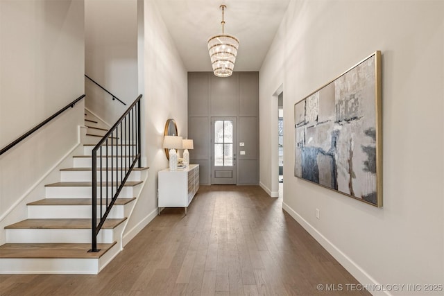 entryway featuring wood-type flooring, a towering ceiling, and an inviting chandelier