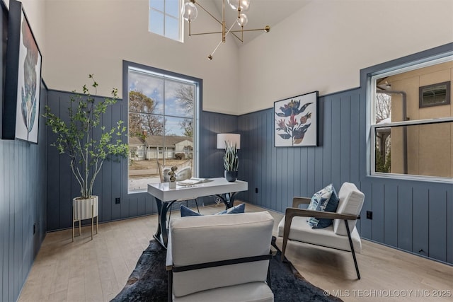 office space featuring light wood-type flooring, a towering ceiling, and a notable chandelier