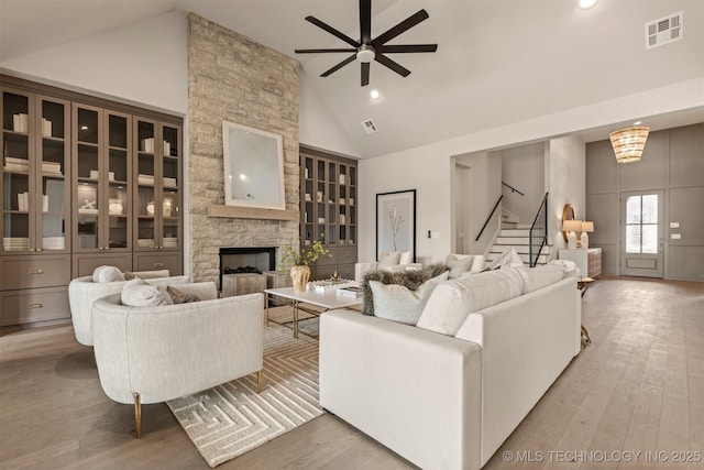 living room featuring ceiling fan, light hardwood / wood-style floors, high vaulted ceiling, and a fireplace