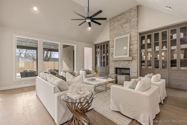 living room with ceiling fan, light wood-type flooring, a fireplace, and high vaulted ceiling