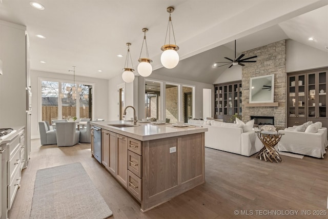 kitchen featuring pendant lighting, a stone fireplace, sink, vaulted ceiling, and a center island with sink