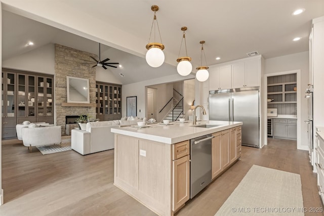 kitchen with pendant lighting, stainless steel appliances, a fireplace, vaulted ceiling with beams, and a center island with sink