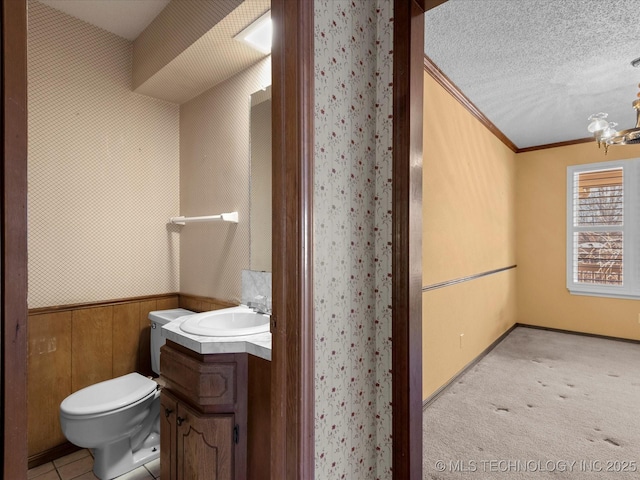 bathroom with toilet, wooden walls, a textured ceiling, ornamental molding, and vanity