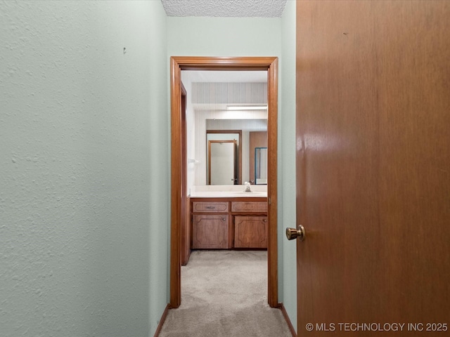 hallway featuring sink, a textured ceiling, and light carpet