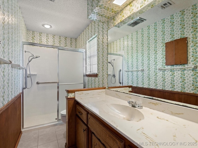 bathroom with a textured ceiling, tile patterned floors, vanity, toilet, and walk in shower