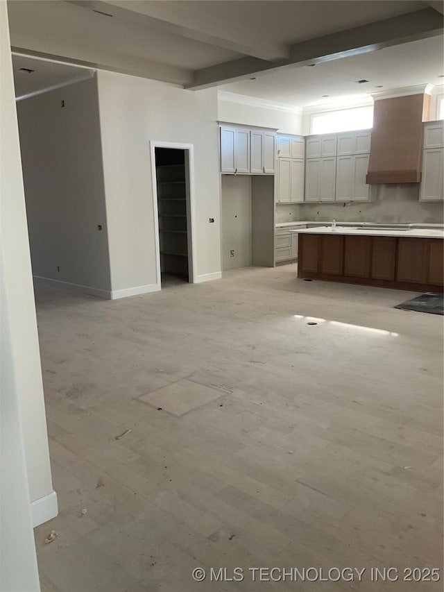 kitchen with wall chimney exhaust hood, a kitchen island, stovetop, white cabinetry, and beamed ceiling