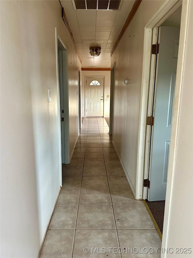 hall featuring light tile patterned flooring, crown molding, and wood walls