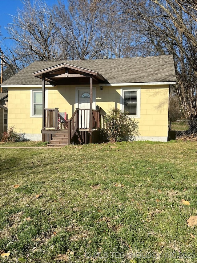 view of front of home with concrete block siding, a front lawn, and a shingled roof