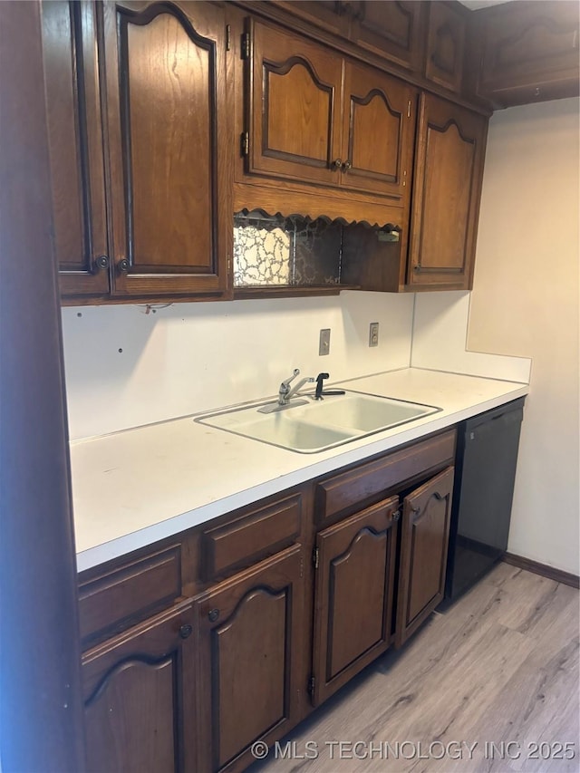 kitchen featuring sink, dark brown cabinetry, black dishwasher, and light wood-type flooring