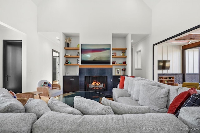 living room with a high ceiling, a tile fireplace, and built in shelves