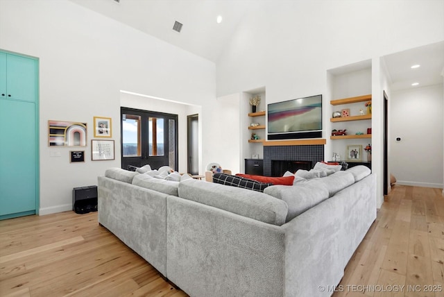 living room featuring high vaulted ceiling, light wood-type flooring, built in features, and a fireplace