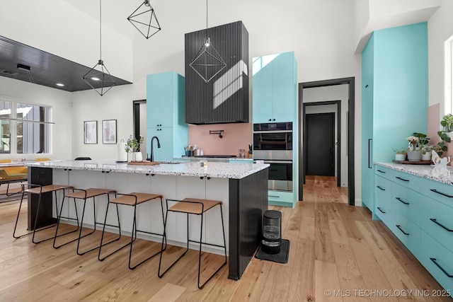 kitchen with pendant lighting, a kitchen island with sink, light wood-type flooring, light stone counters, and blue cabinets